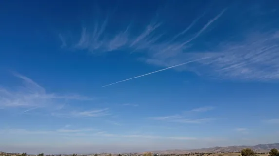 Pure clear sky at midday with intense cobalt blue tones, wispy cirrus clouds forming delicate brush strokes across the expanse, single contrail from aircraft creating