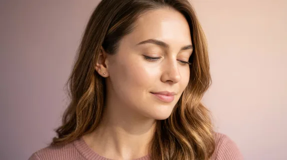 Close-up portrait of a woman with glowing skin and minimal makeup, her face angled toward soft directional light, gradient background shifting smoothly from dusty mauve