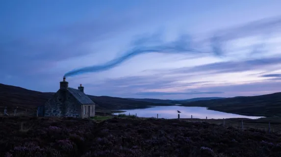 A Highland Scottish moorland at blue-dusk, a crofter's chimney releasing a thin thread of blue peat smoke that rises and bends in the wind, the surrounding heather dark purple in the fading light,