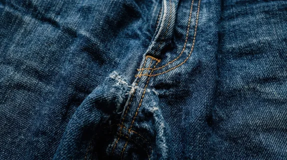 Crumpled blue denim texture filling the entire frame, deep indigo fabric with visible stitching and worn cotton fibers, natural creases and folds creating dramatic