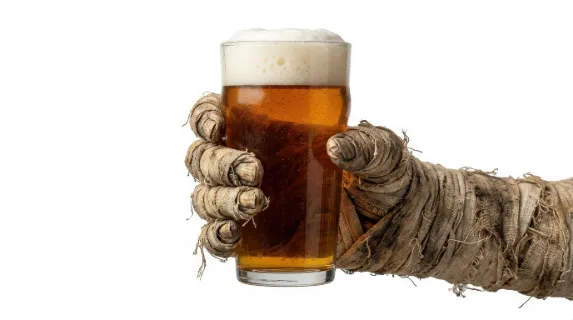 A mummy hand wrapped in aged bandages holding a glass of beer topped with foam, isolated on white background, quirky spooky party concept with sharp studio detail, ultra-realistic, no logos.
