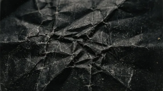 A crumpled black paper surface with scratches and dust, distressed folds, gritty texture and aged photographic wear, dark editorial mood, ultra-realistic, no logos.