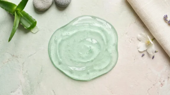 A smooth transparent light green gel puddle seen from above on a pastel background, fresh aloe-like texture and soothing natural spa mood, ultra-realistic, no logos.