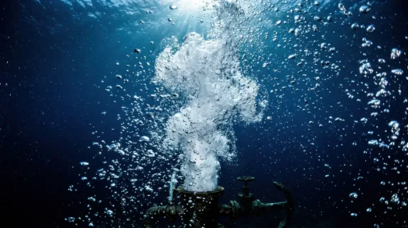 Underwater explosion of air bubbles released from a submerged source, thousands of spheres of varying sizes racing upward in a turbulent column, each bubble catching and