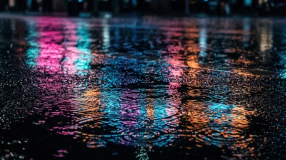 Neon light reflections shimmering across a wet urban street surface at night, electric pink and cyan streaks stretching and rippling in shallow puddles, rain droplets