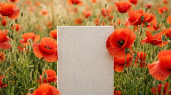 a tight focus on the blank paperback cover surrounded by radiant red poppies, capturing the gentle textures of the linen. the vibrant colors radiate warmth in the hazy