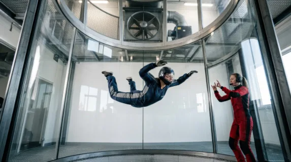 A vertical wind tunnel facility with a skydiver in freefall formation training, the body fully arched and delta-shaped in the center of the glass tube, fabric suit and
