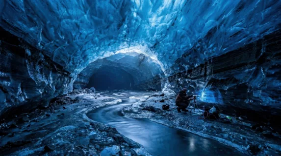 A glacier cave interior discovered beneath a retreating ice sheet, the ceiling a dome of compressed blue ice so dense it absorbs all red wavelengths leaving the space in