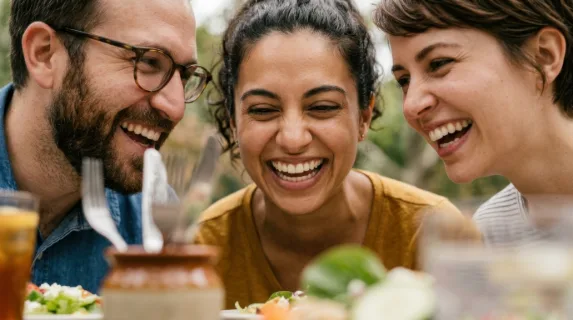 an intimate close-up of joyful faces as coworkers share laughter over a light lunch on a rustic picnic table. the camera focuses tightly on their expressions, showcasing