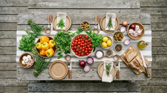 an overhead view of the rustic table brimming with vibrant culinary ingredients, including bright red tomatoes, soft yellow bell peppers, and fresh greens. the