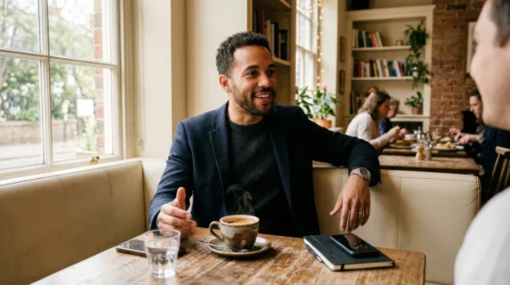 a 32-year-old mixed-race male consultant engaged in a candid conversation at a cozy cafe corner, with a steaming cup of rich espresso on the table. the environment