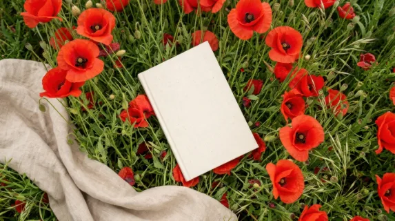 an overhead view of the blank paperback cover nestled among vibrant red poppies and soft linen, emphasizing the dynamic angle of the cover. the lush green grass creates a