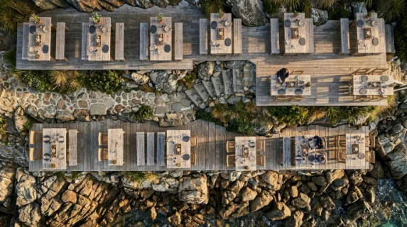a distinct overhead angle featuring the terraced tables on the shore, crafted from natural materials and adorned with artisanal slate coasters and rustic wooden trays