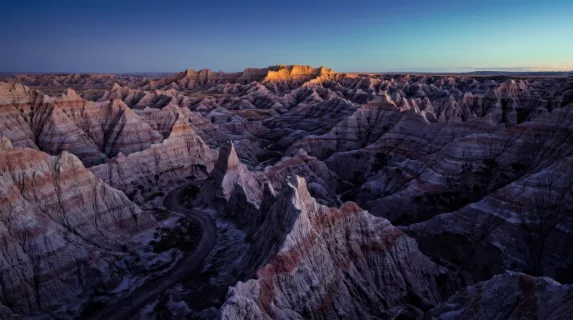 A dramatically eroded badlands landscape at blue hour, thousands of pointed clay pinnacles in banded layers of lavender, grey and terracotta extending to every horizon,
