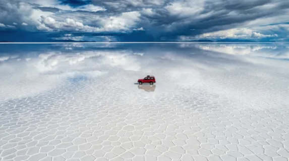 An aerial drone view of a perfect geometric salt flat stretching to every horizon, blinding white hexagonal mineral formations covering the ground in a natural mosaic, a