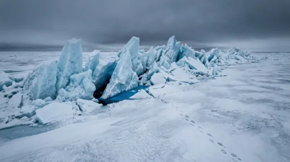 An Arctic pressure ridge at midday, enormous slabs of sea ice forced vertically by tectonic collision of ice sheets, jagged translucent blue turrets rising four meters