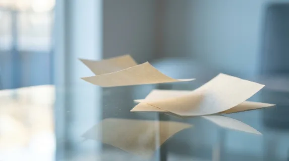 an intimate close-up of papers gracefully drifting over a clear, reflective surface that mirrors the surrounding soft light. the focus highlights the playful, surreal