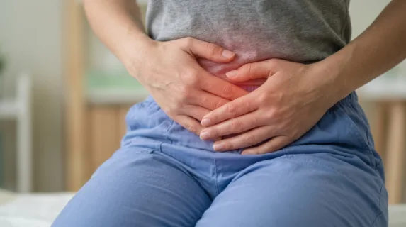 Close-up of a person holding their abdomen with a highlighted area indicating stomach pain, subtle red glow effect suggesting discomfort, neutral background softly