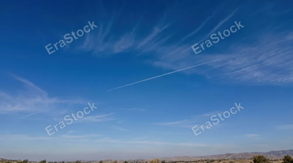 Pure clear sky at midday with intense cobalt blue tones, wispy cirrus clouds forming delicate brush strokes across the expanse, single contrail from aircraft creating