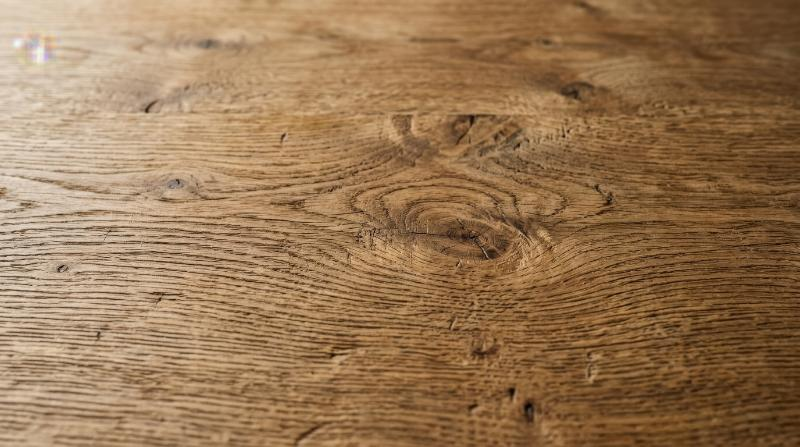 A natural wooden surface with visible grain, warm organic lines and subtle knots, timeless rustic texture background, ultra-realistic, no logos.