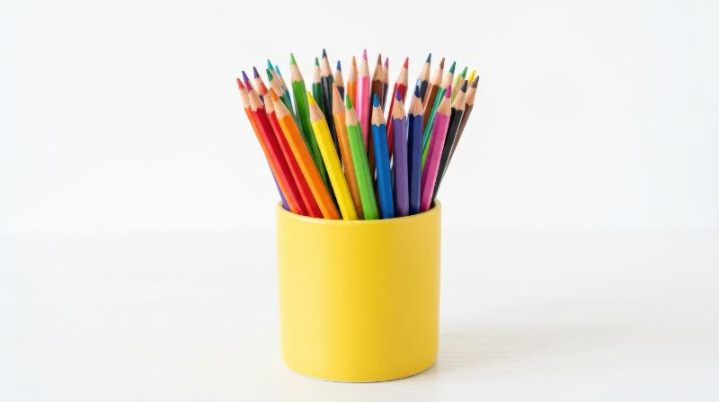 A set of colored pencils standing upright in a bright yellow holder against a clean white background, sharp tips and vivid hues, cheerful creative atmosphere, ultra-realistic, no logos.