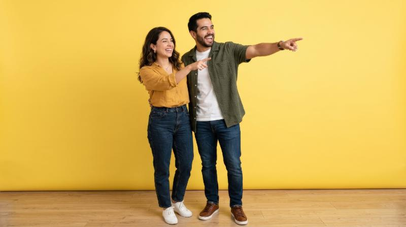 A happy Latino couple pointing outward against a yellow background, cheerful expressions, casual stylish clothing, clean bright studio mood, ultra-realistic, no logos.