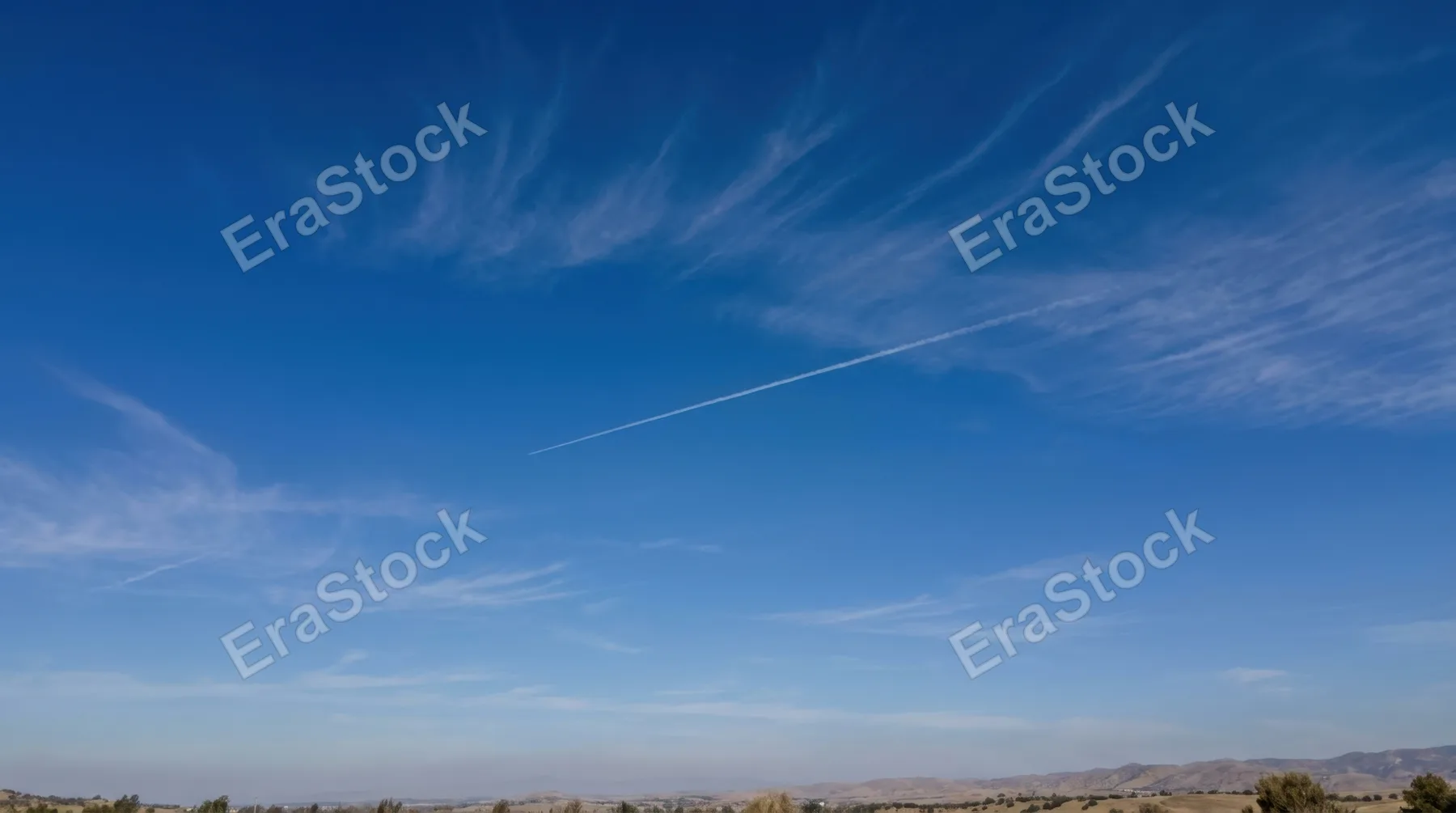 Pure clear sky at midday with intense cobalt blue tones, wispy cirrus clouds forming delicate brush strokes across the expanse, single contrail from aircraft creating