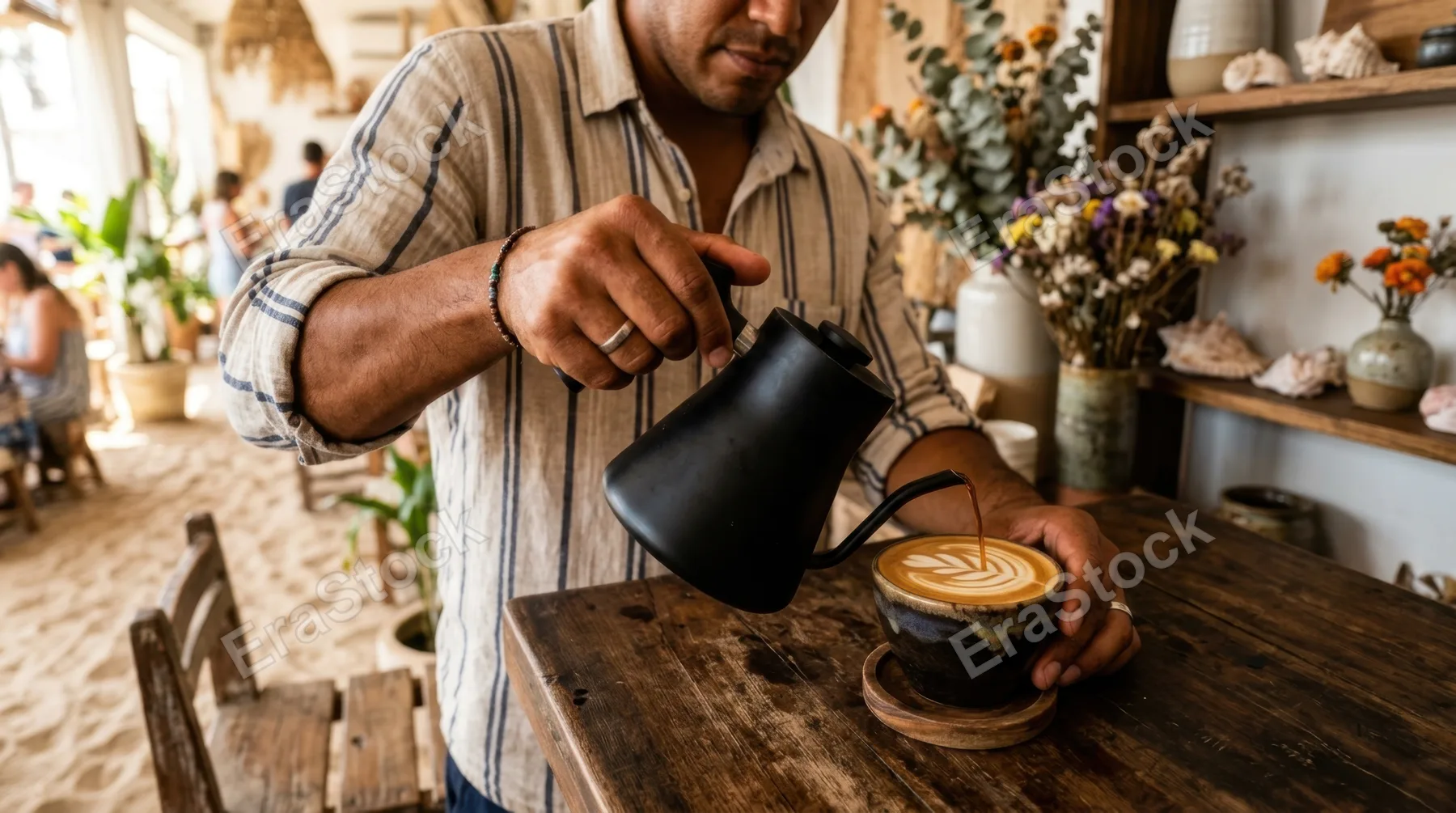 a close-up detail of a hispanic male baristas hands gracefully pouring coffee into a cup, capturing the textural nuances of his casual summer outfit and the sandy cafe