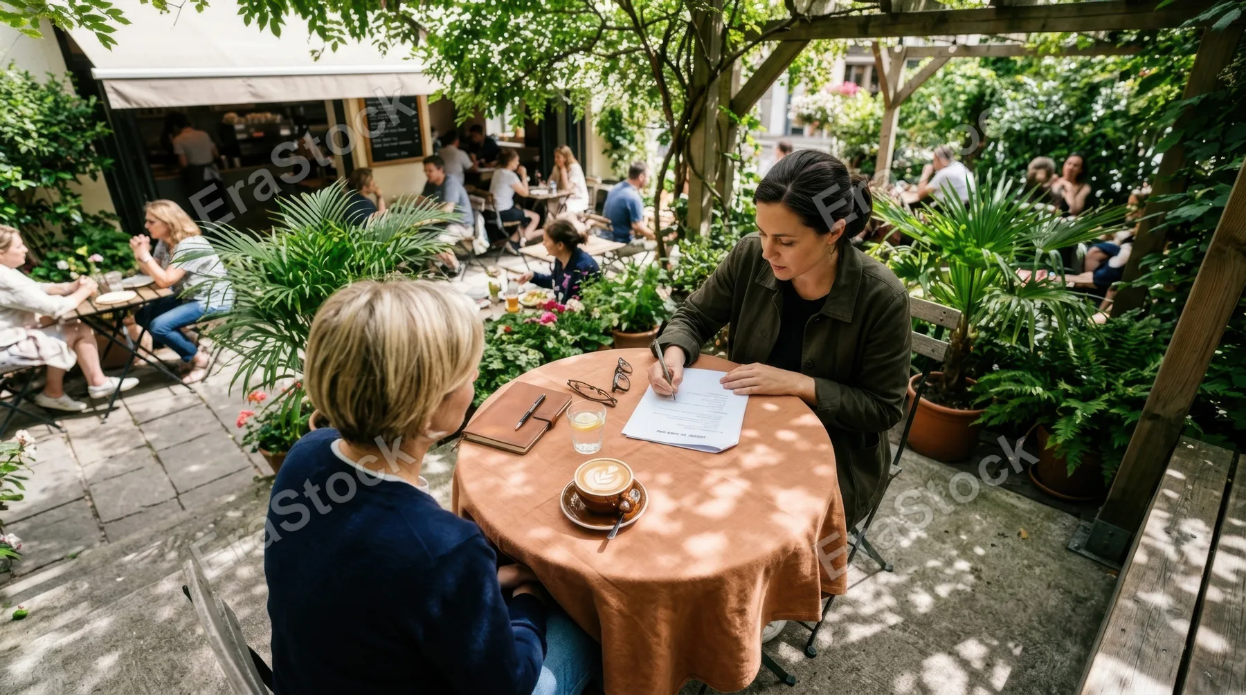 an overhead angle showing the director at the cafe table with the flat white prominently showcased alongside the muted orange tablecloth, giving context to the vibrant