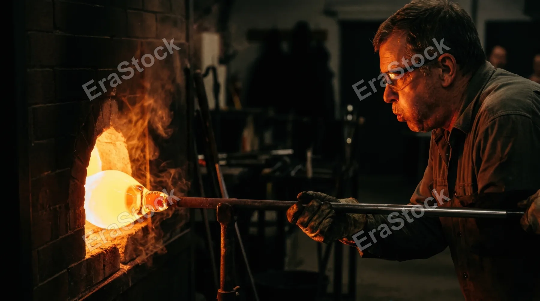 A master glassblower gathering molten glass on a blowpipe from a furnace mouth, the gather glowing from inside at 1200 degrees, the blower's cheeks inflated mid-breath,