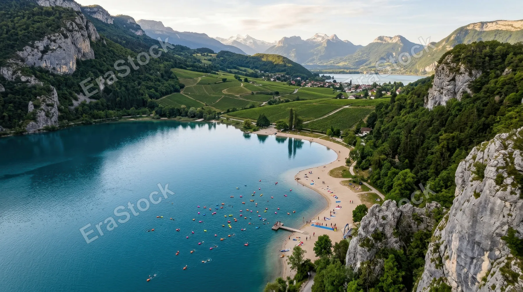 a distinct overhead angle capturing the tranquil mountain lake and colorful tow floats, framed by rocky gray cliffs and sandy beige lakeshore that seamlessly blends into