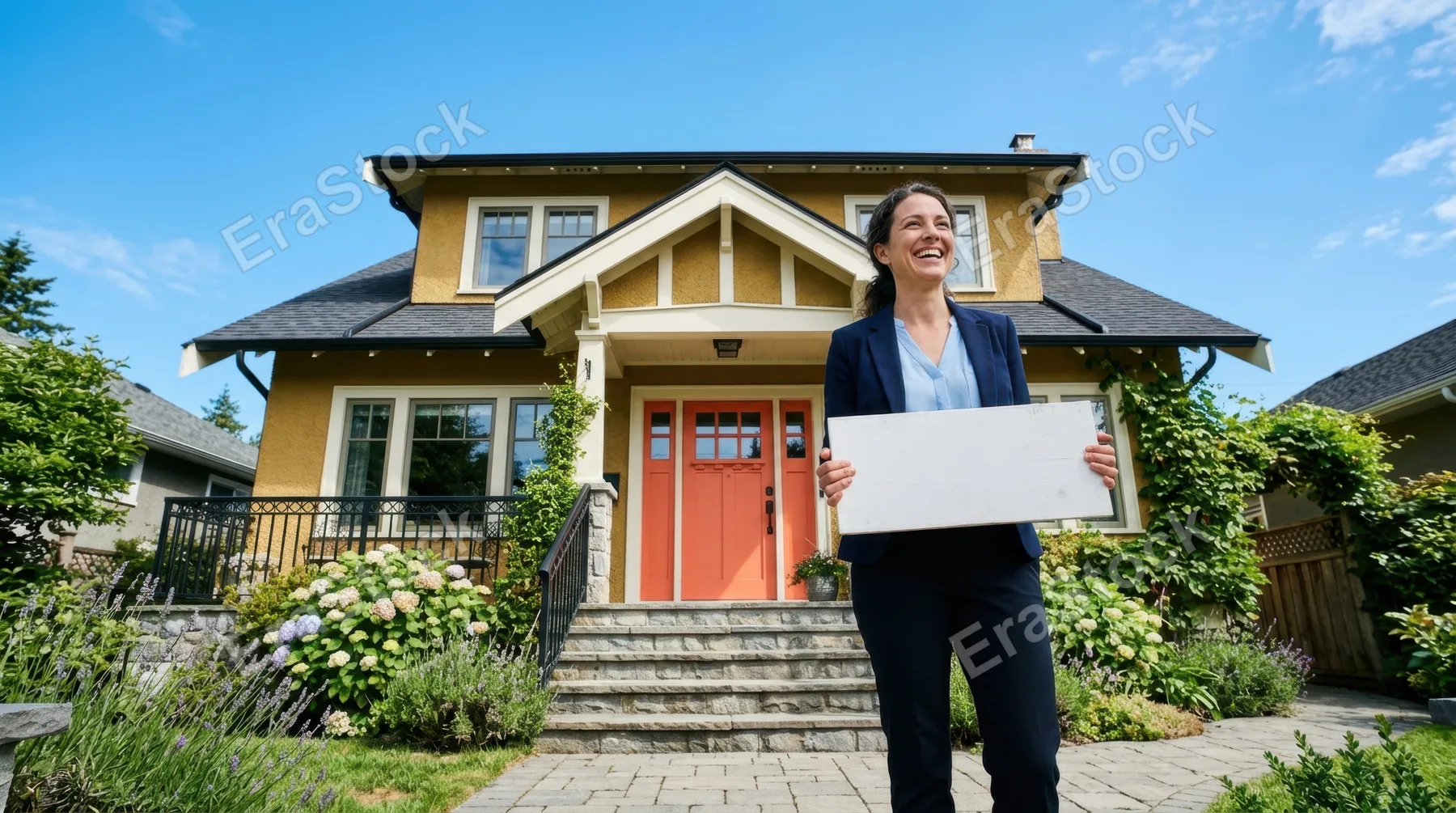 a low-angle shot of the realtor smiling while holding the blank sign, with the house and its coral door towering above her in a candid moment, set against a clear blue