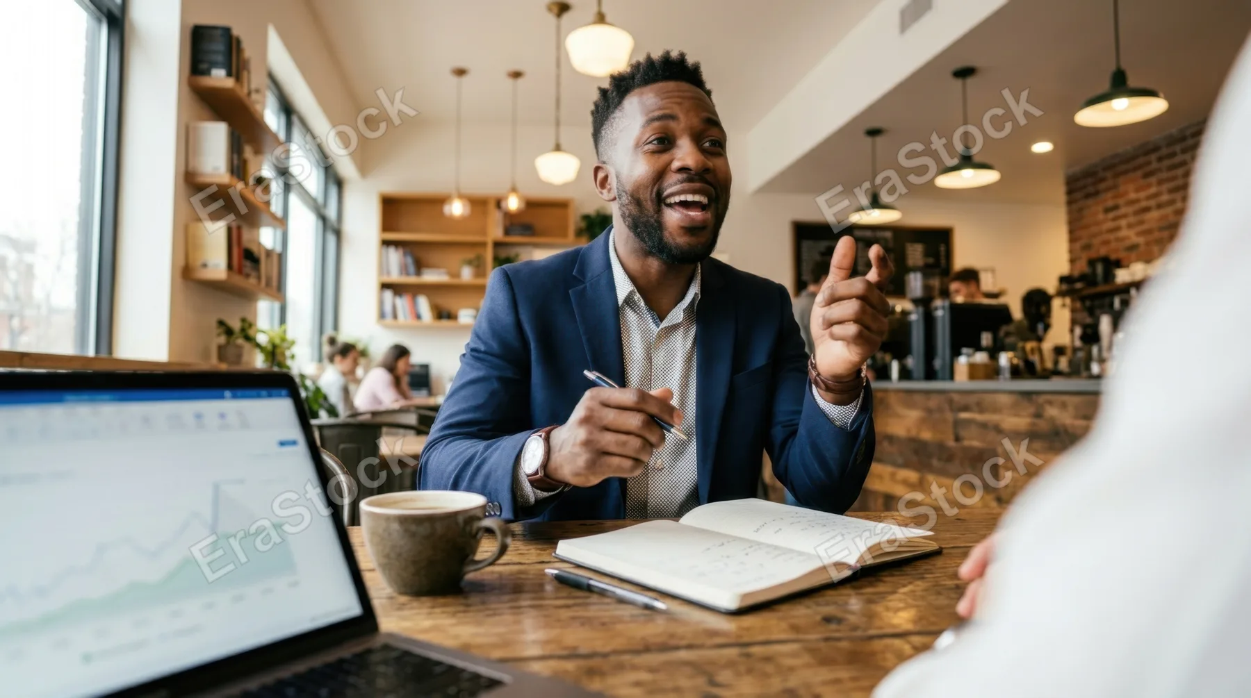 a low angle view of the 30-year-old black male project manager in the coworking space, emphasizing his engagement and body language during the conversation, with cozy caf