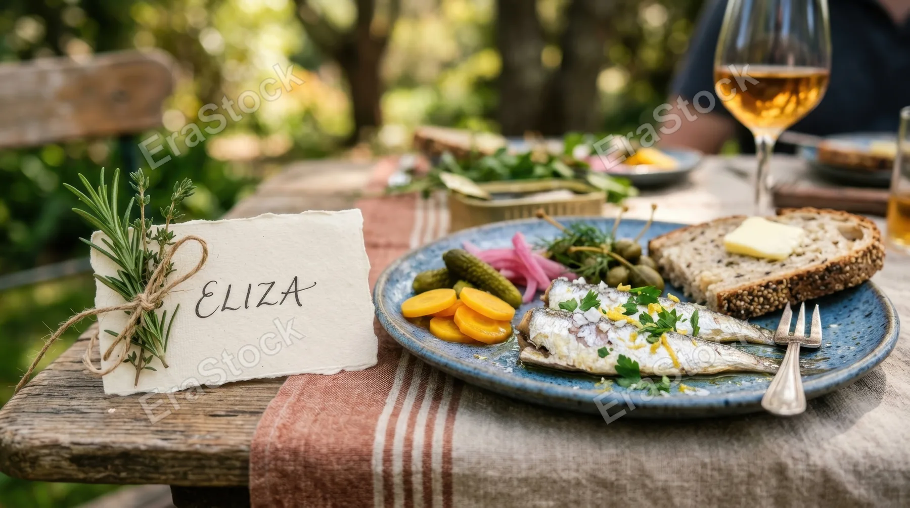 a close-up of a handwritten name tag next to a beautifully arranged plate of tinned fish and pickles, highlighting the craftsmanship of the picnic setup. the gentle,