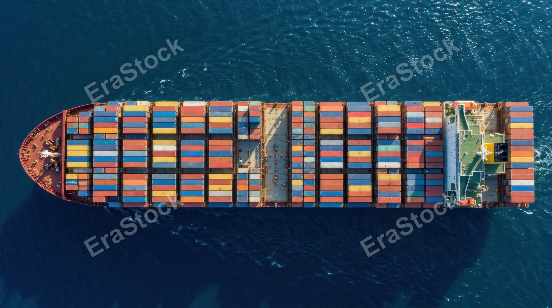 A cargo ship deck loaded with colorful stacked shipping containers stretching the full length of the vessel, seen from directly above, geometric patterns formed by the