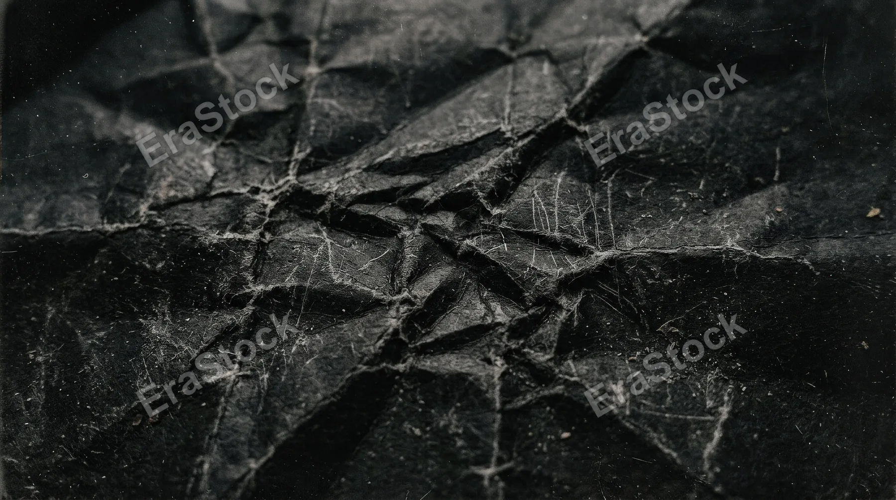 A crumpled black paper surface with scratches and dust, distressed folds, gritty texture and aged photographic wear, dark editorial mood, ultra-realistic, no logos.