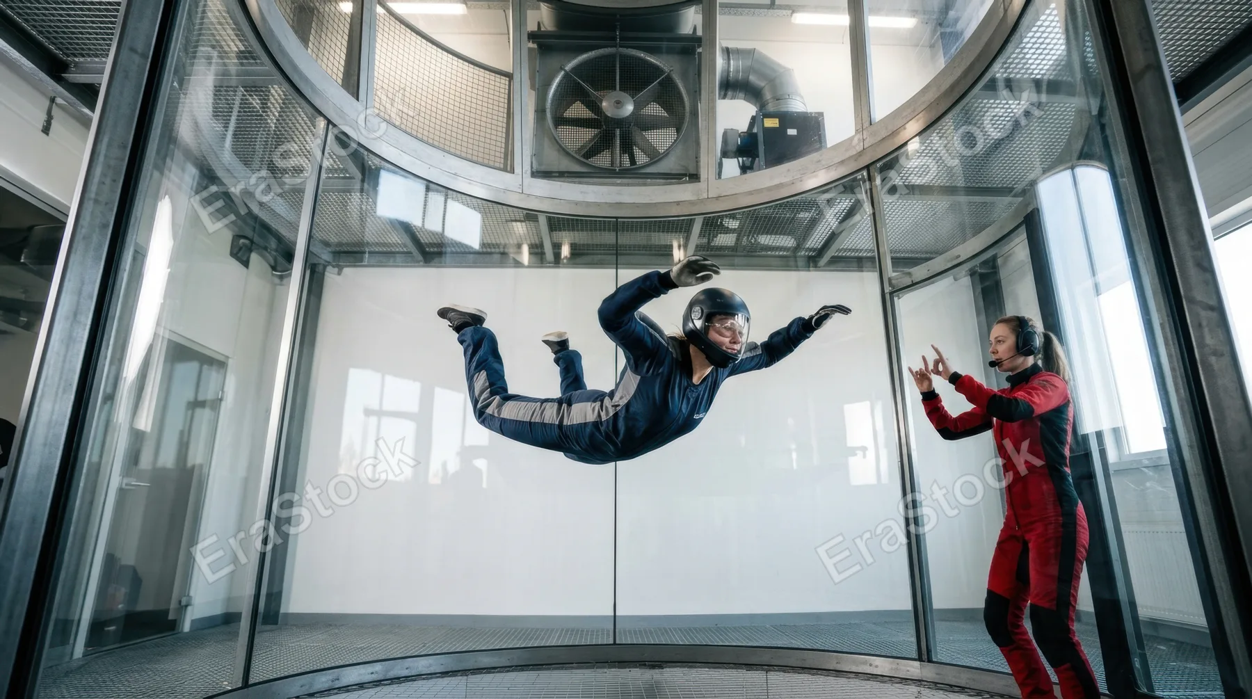 A vertical wind tunnel facility with a skydiver in freefall formation training, the body fully arched and delta-shaped in the center of the glass tube, fabric suit and