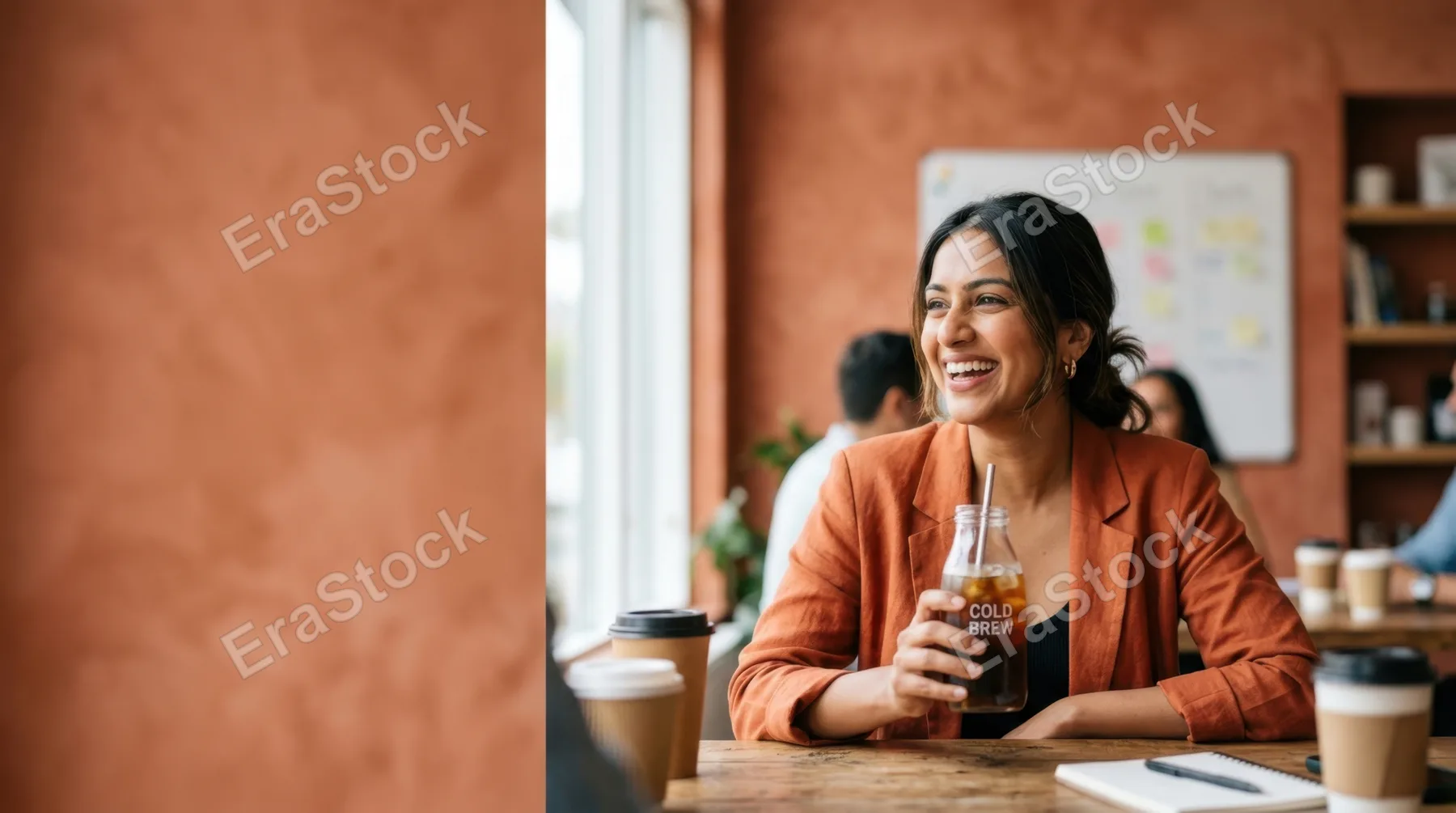 a bold and clean composition showcasing a 30-year-old south asian female team leader in the lower right quadrant, smiling while holding a cold brew coffee during a