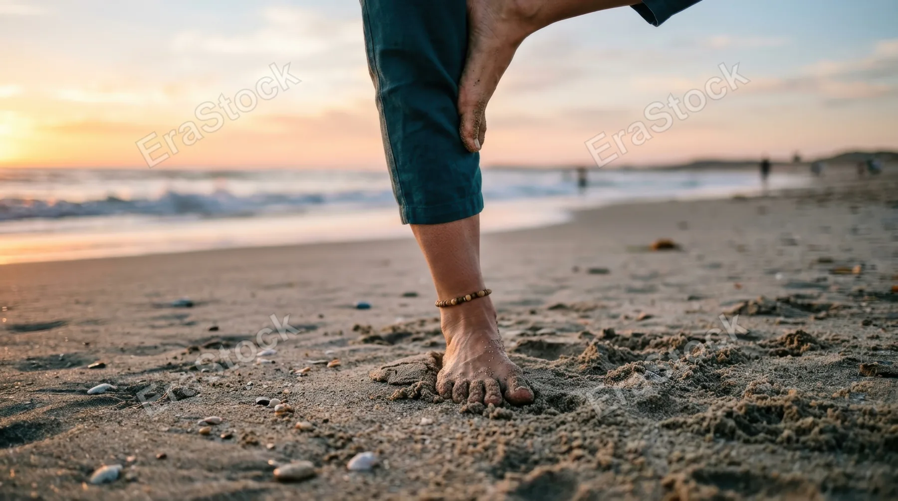 a close-up view of the instructor's foot and leg as she performs a yoga pose on the sand, showcasing the dynamics of her movement and the texture of the beach. this