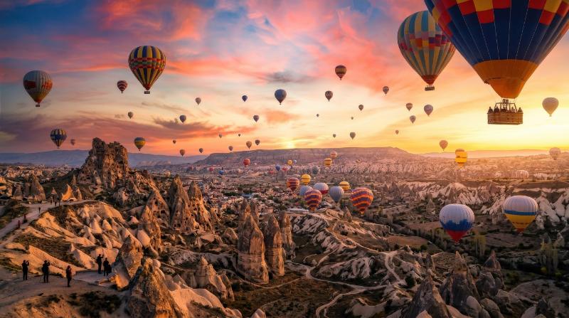 Vibrant hot air balloons soaring above the iconic rock formations of Cappadocia, glowing sky, tourism adventure spirit, breathtaking travel atmosphere, ultra-realistic, no logos.