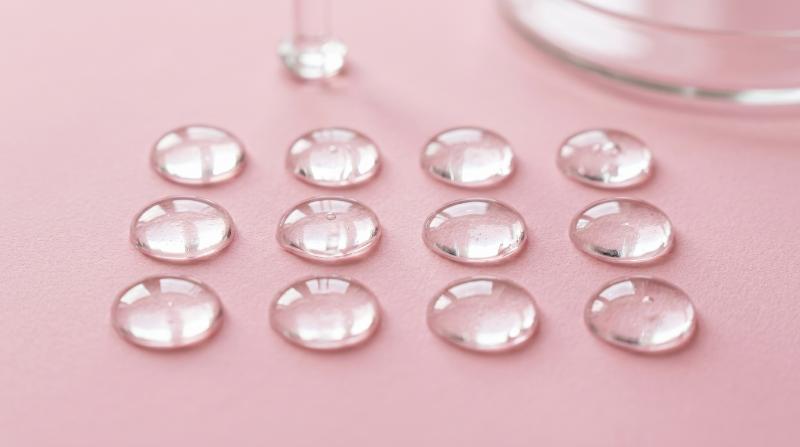Round serum oil samples on a pink background, glossy gel texture with hyaluronic-inspired clarity, clean cosmetic testing aesthetic and soft feminine mood, ultra-realistic, no logos.