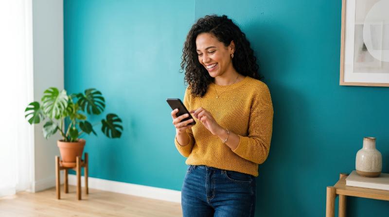 A woman using a smartphone while smiling near a teal wall, clean composition, natural pose, vivid color contrast and a fresh contemporary lifestyle mood, ultra-realistic, no logos.