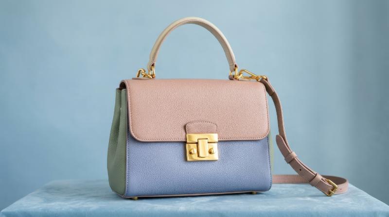 A stylish handbag with pastel-colored panels and polished gold hardware set against a simple blue background, soft studio light and refined fashion mood, ultra-realistic, no logos.