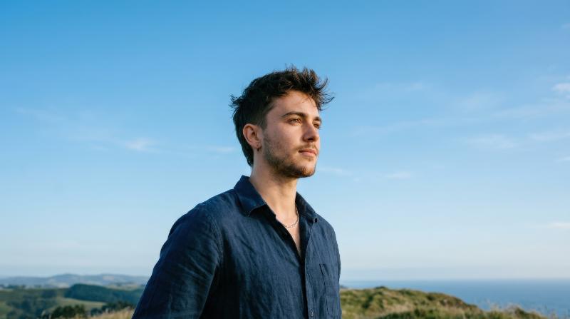 Low-angle portrait of a thoughtful transgender person looking away against a clear blue sky, natural light, clean composition, quiet confidence and openness, ultra-realistic, no logos.