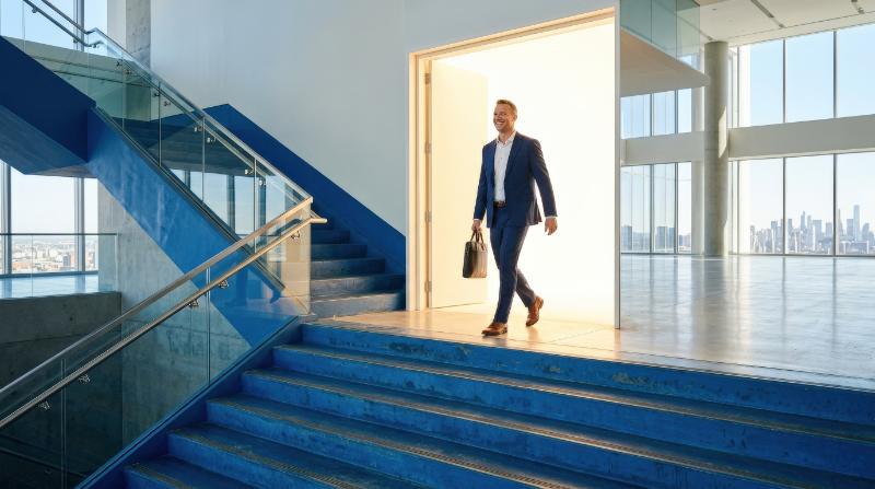A man walking through a bright open doorway at the top of a large blue staircase, glowing threshold, clean expansive space, triumphant career transition and final success mood, ultra-realistic, no